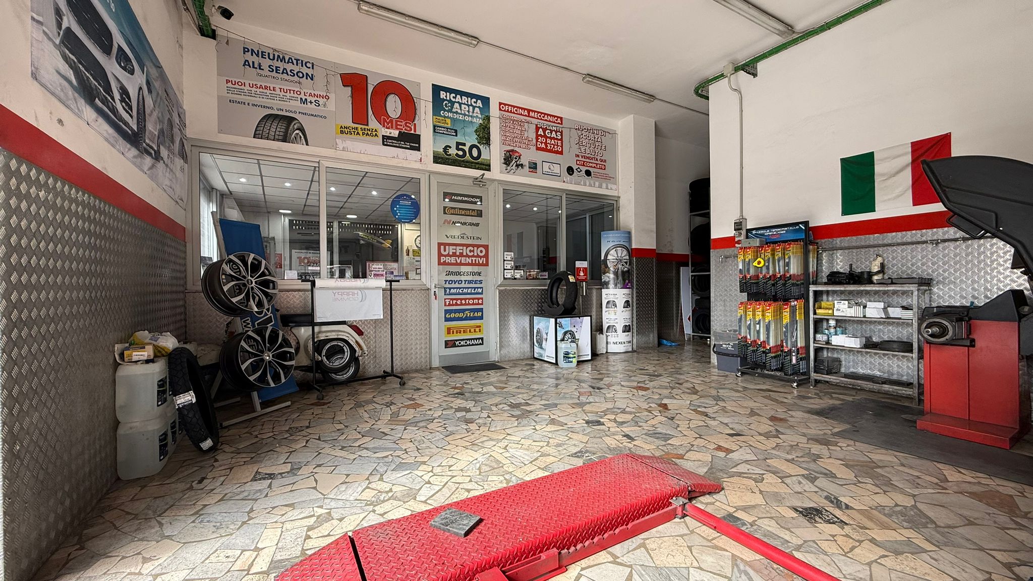 Interno dell'officina con ponte rosso e postazioni operative sullo sfondo